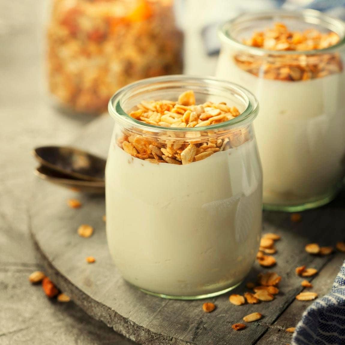 Homemade granola muesli with nuts and dried fruits and yogurt in glasses on rustic stone background