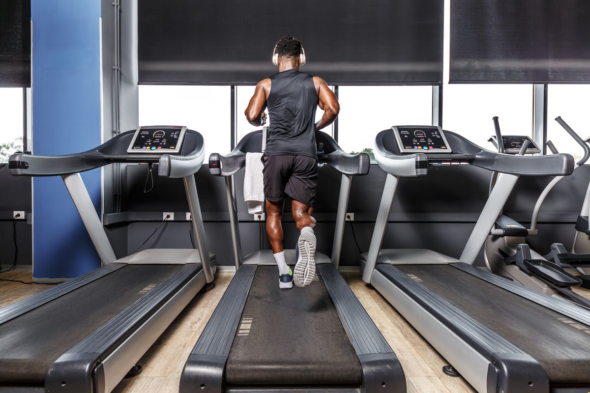 A man is energetically running on a treadmill in a gym. The gym is well-lit and equipped with various exercise machines, including the treadmill.