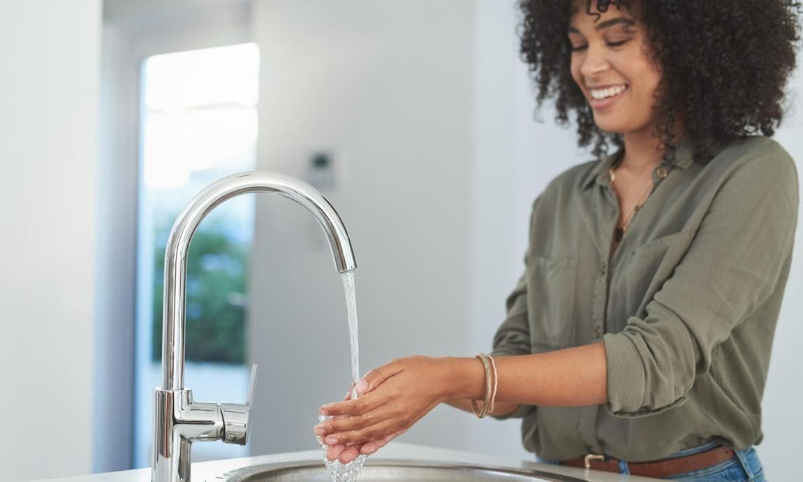 Shot of a young woman washing her hands at the kitchen sink