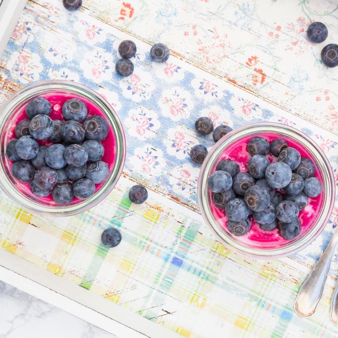 Two glasses of overnight oats with blueberries and berry juice on a wooden tray