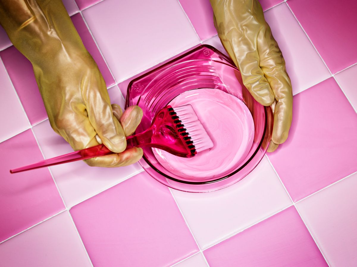 hand with gloves preparing pink hair tint and pink tiles as surface