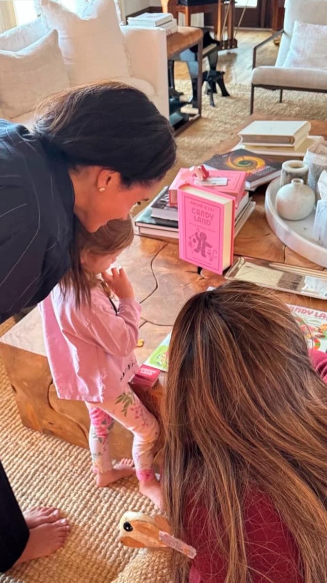 Meghan Markle, Serena Williams, and Lilibet Diana playing Candy Land together in a cozy home setting.