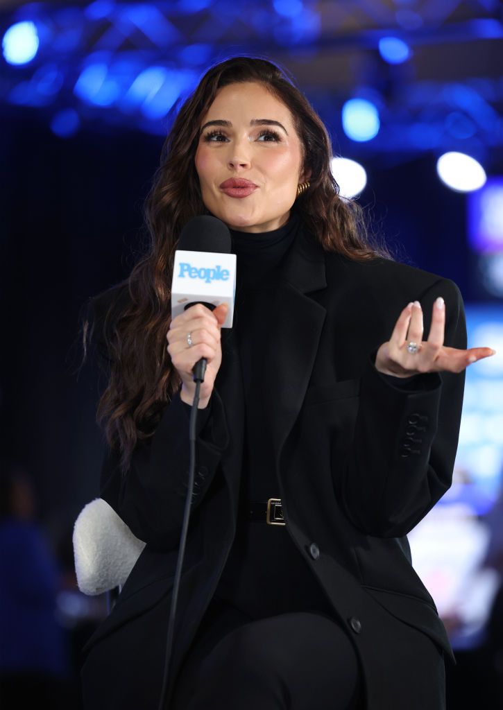 Olivia Culpo speaking into a microphone during a People interview at a Super Bowl event.