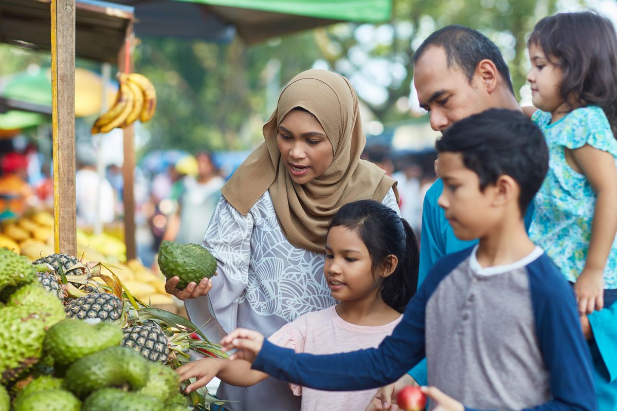 Family of five buying soursop in market. 