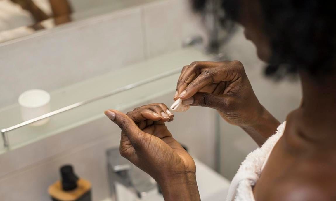 Unrecognizable African female removing her nail polish.