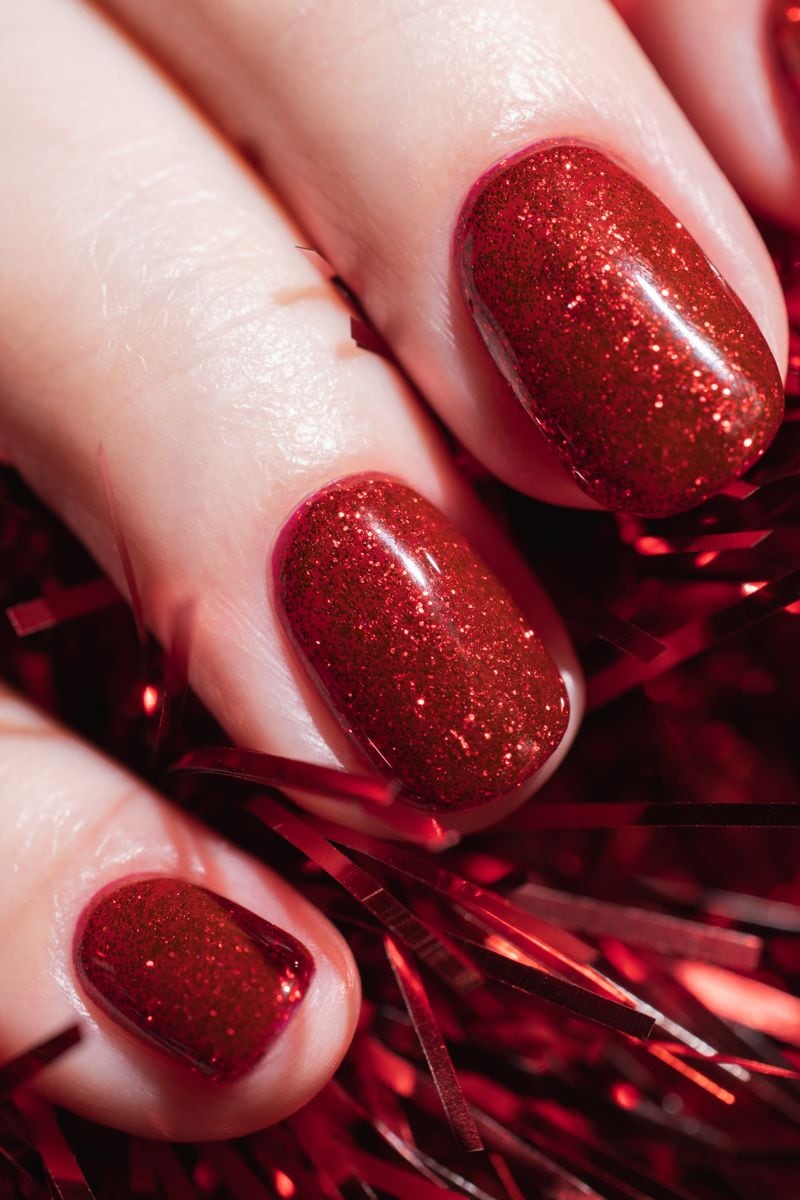 Female hand with beautiful holiday manicure - red glitter gel nails with Christmas tinsel. Nail care concept