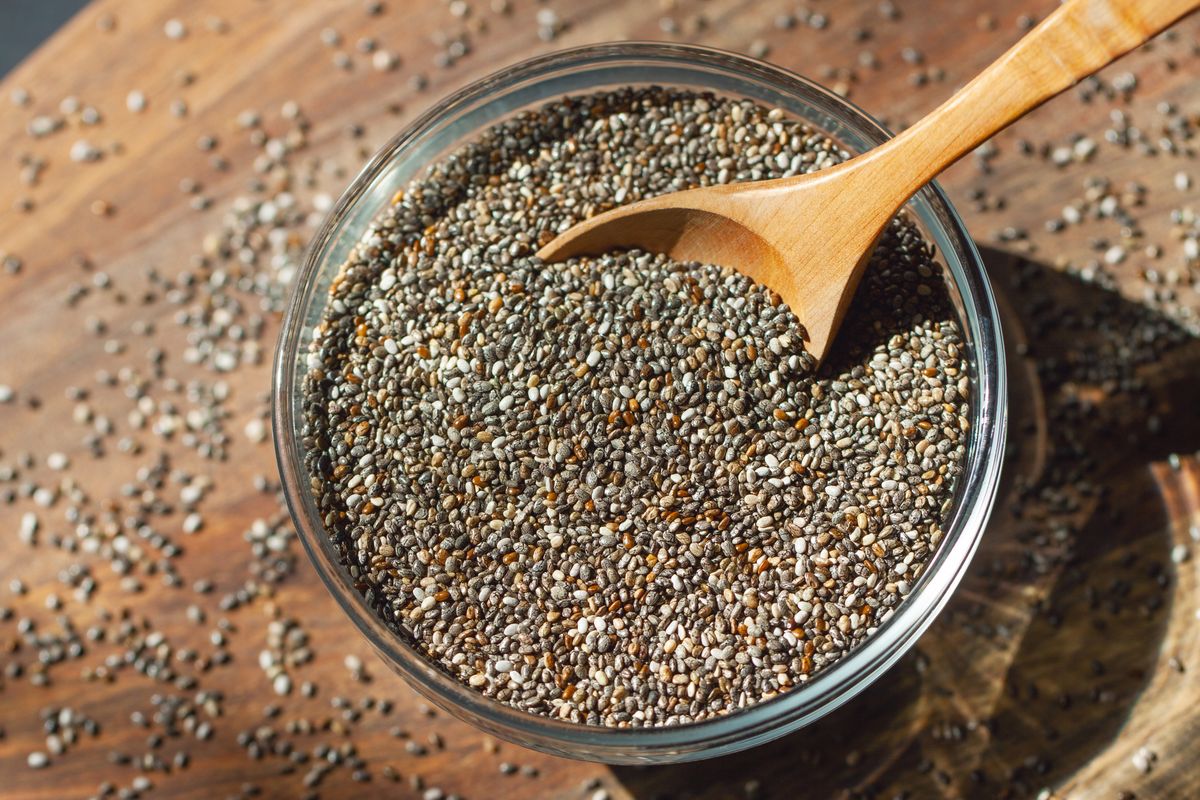 Chia seeds in a glass bowl with a spoon. Wooden board as a background. Healthy food concept, superfood, dietary supplements. 