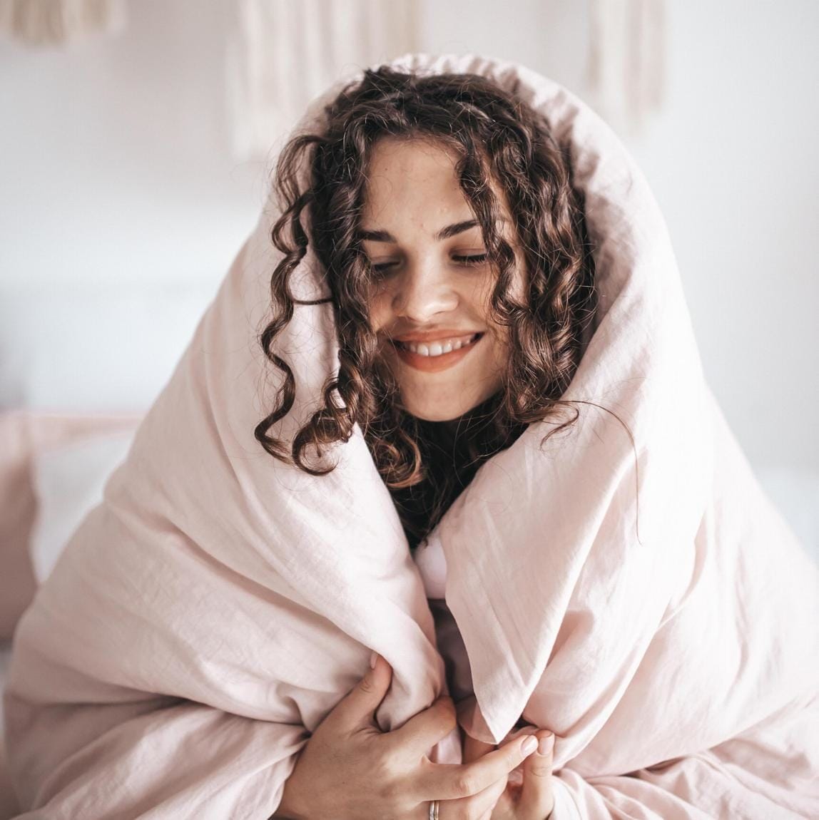 Curly haired person waking up wrapped in covers.