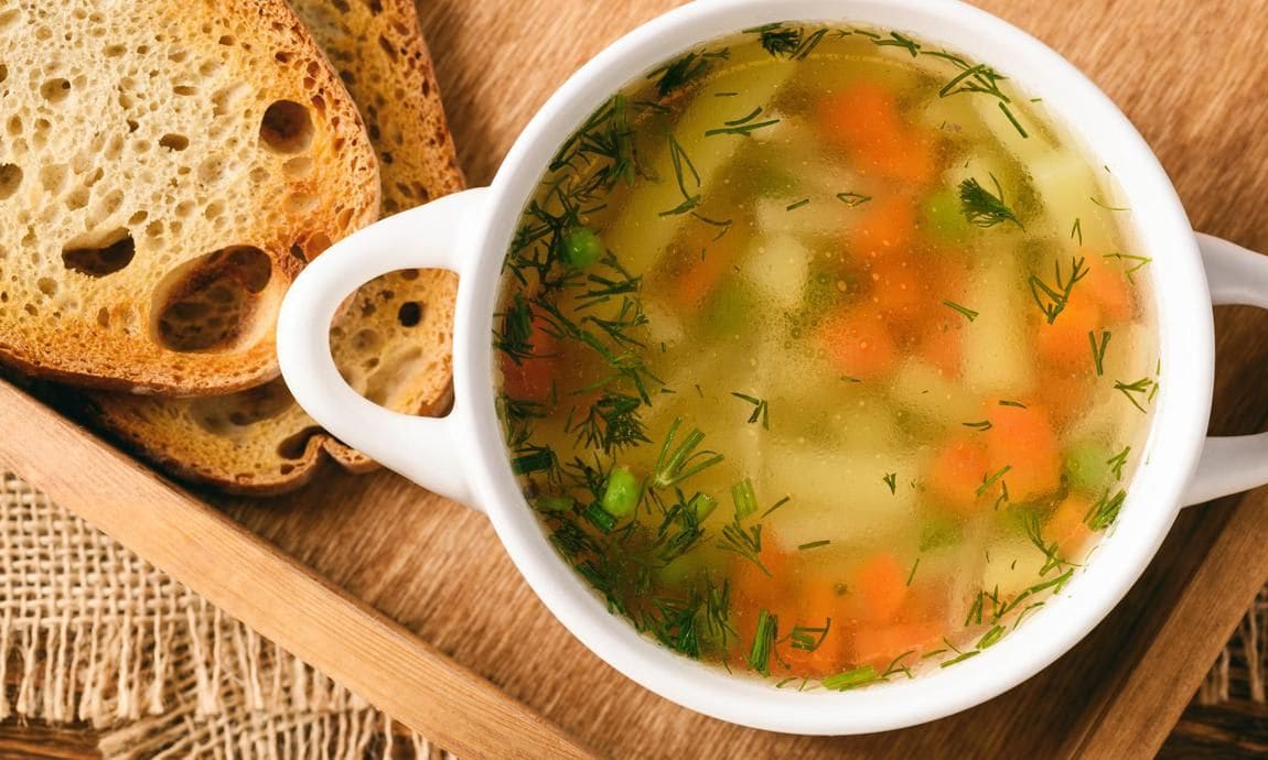 Chicken soup in a white bowl on top of a wooden tray.