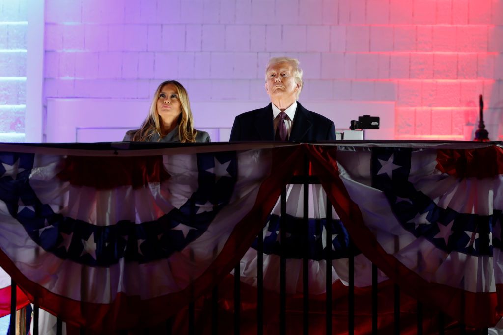 Donald Trump and Melania Trump are standing behind a railing draped in patriotic red, white, and blue bunting. watching the fireworks show at Trump National Golf Club 