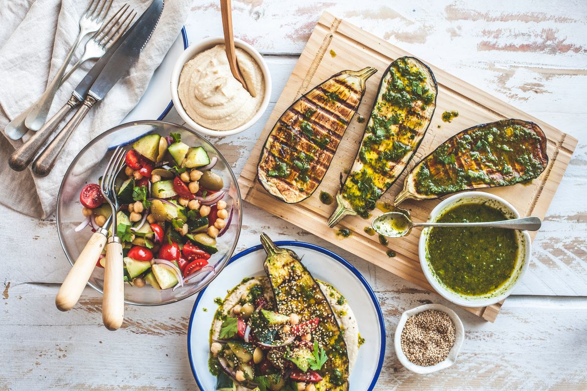 Una variedad colorida y fresca de berenjena/berenjena a la parrilla con ensalada, mantequilla de hierbas y puré de frijoles. ¡Una comida equilibrada y saludable para veganos, vegetarianos o amantes de las verduras!