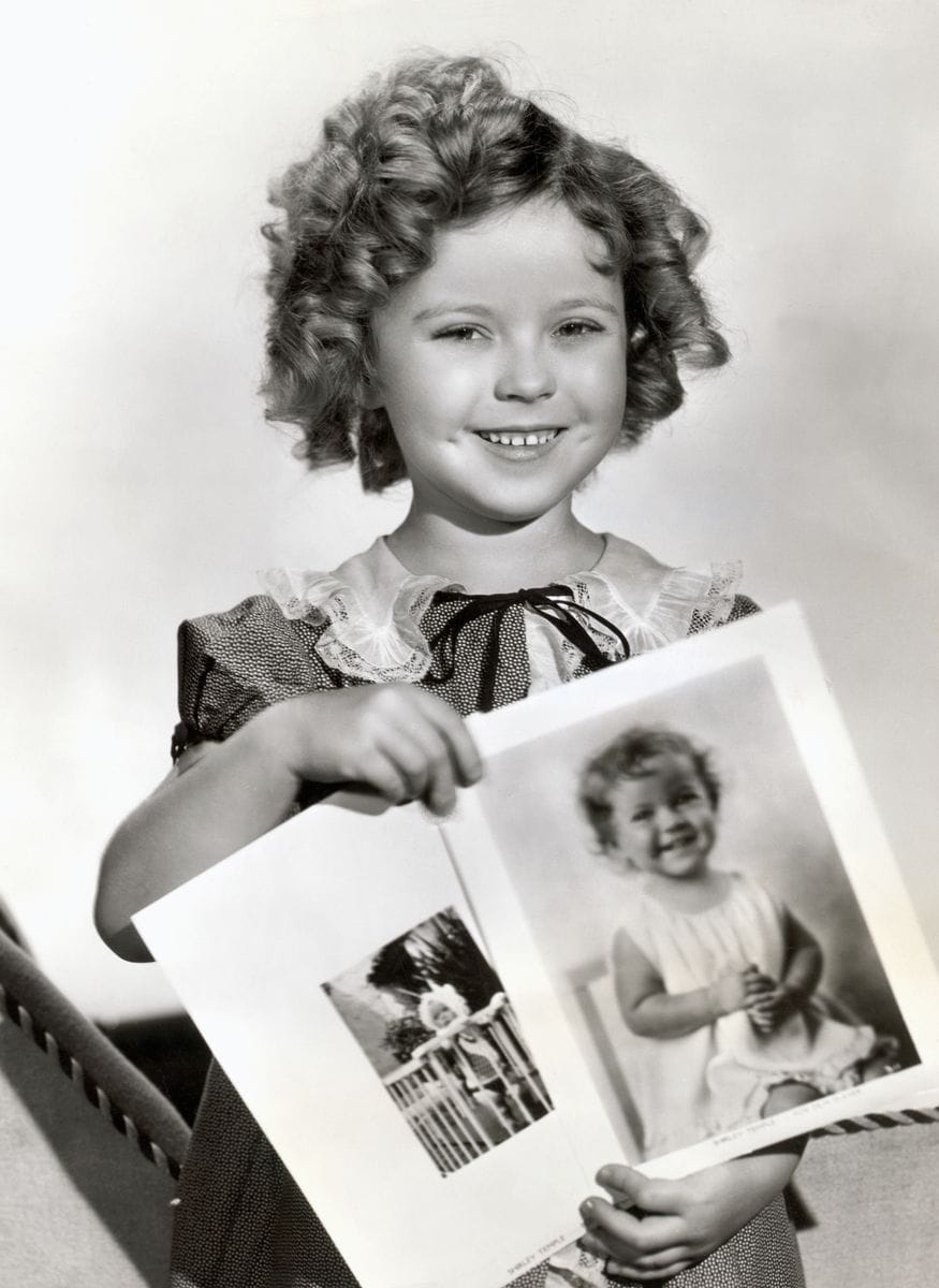 Photograph of Shirley Temple, ca. 1935, holding baby pictures of herself.