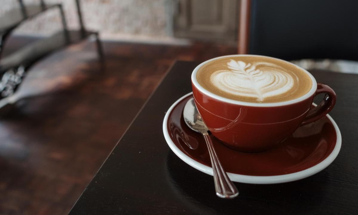 Cappuccino on top with beautiful delicate latte art with leaf pattern, and background of red rough rusty metal table.