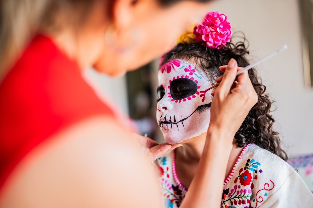 Mother helping daughter to get face makeup as a sugar skull for day of the dead