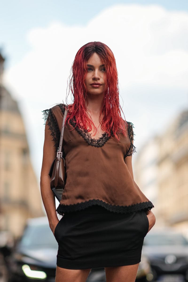 Mara Lafontan wears a dark brown satin black lace trimmed sleeveless shirt, dark brown leather bag, and black mini skirt outside Viktor & Rolf during the Paris Haute Couture Week Fall/Winter 2024-2025 on June 26, 2024, in Paris, France. 