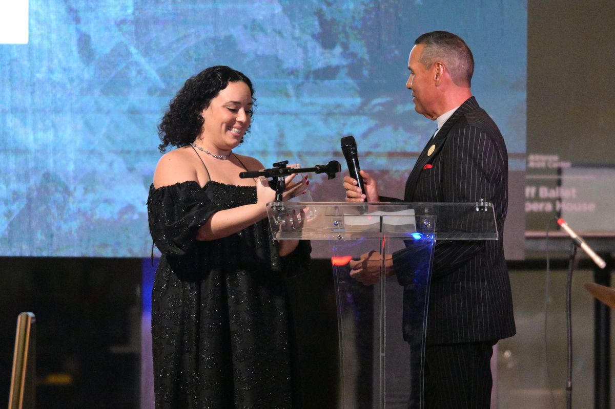 Liana Salinas receiving the Inca Garcilaso Medal from Luis García on stage during a formal awards ceremony.