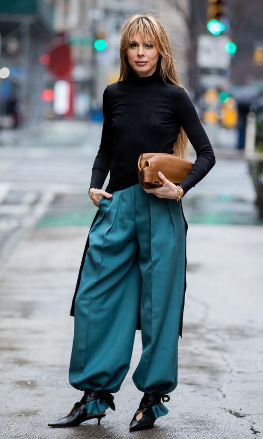 Ekaterina Mamaeva in a black sweater, blue wide-leg pants and black ankle strap sandals tied over the bottom of her pants