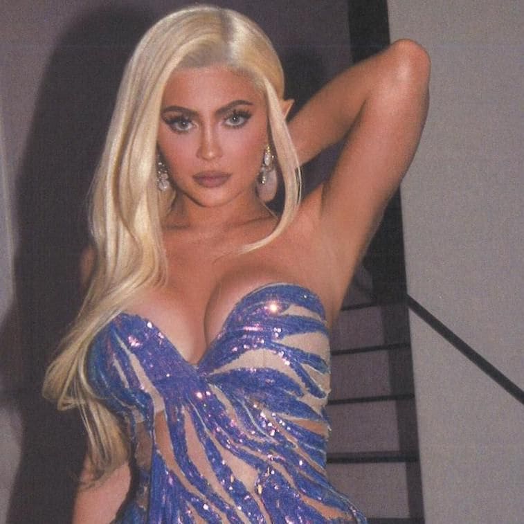 Kylie Jenner poses with long curly blonde hair in a semi-sheer royal blue dress