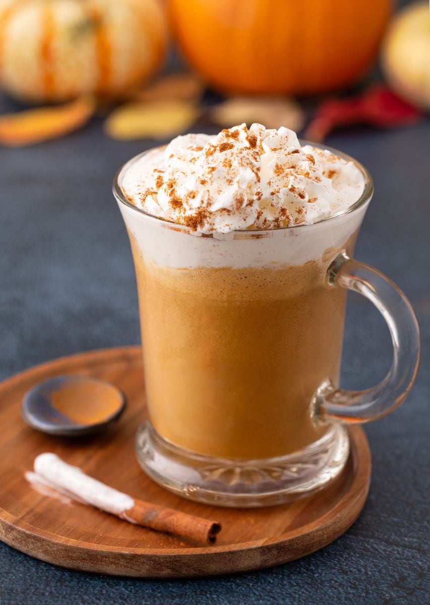 Pumpkin spice latte topped with whipped cream and cinnamon in a glass mug in a wooden plate