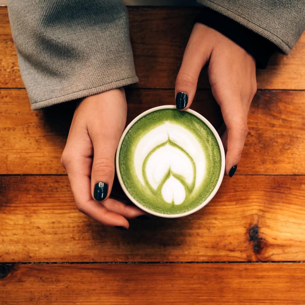 Woman hands hold a ceramic cup with matcha green tea latte