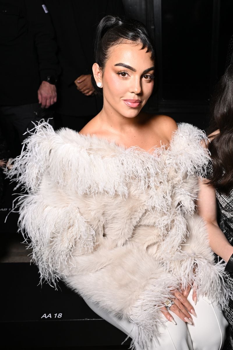 A close-up of Georgina Rodríguez at Paris Fashion Week, wearing a glamorous off-the-shoulder white feathered outfit, with sleek hair and elegant makeup.