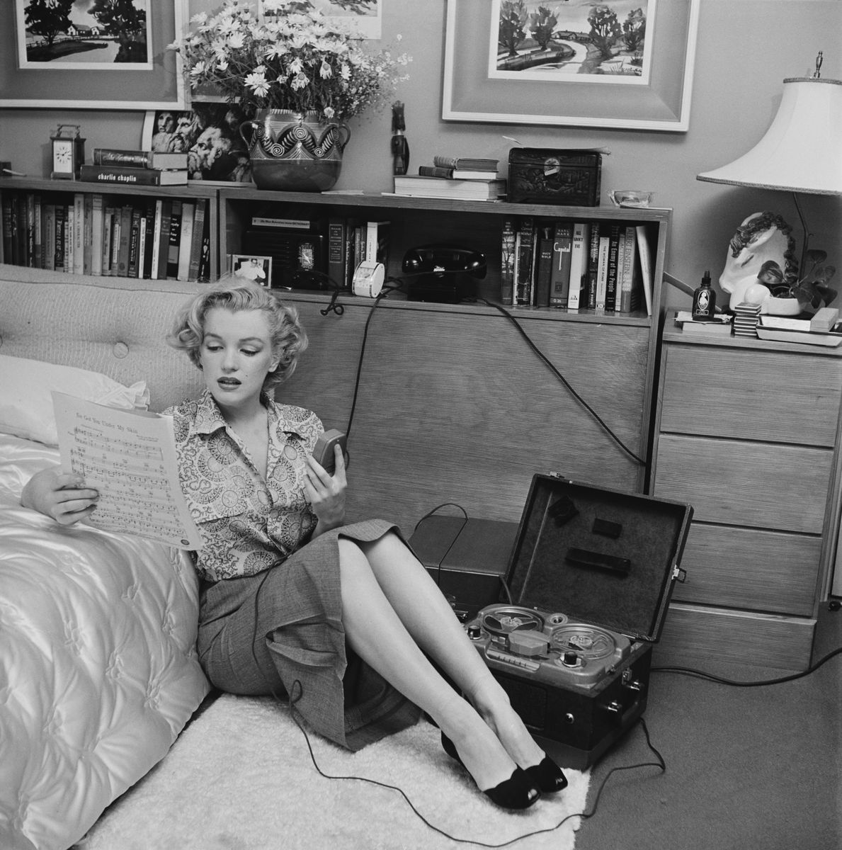 American actress Marilyn Monroe (1926 - 1962) read sheet music while sitting on a bedroom floor with a tape player on the side circa 1950. 