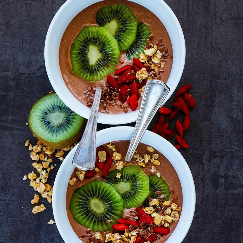 Tasty breakfast bowls of banana and chocolate smoothie, dessert, yogurt or milkshake topped with goji berries, kiwi fruit, seeds and oats