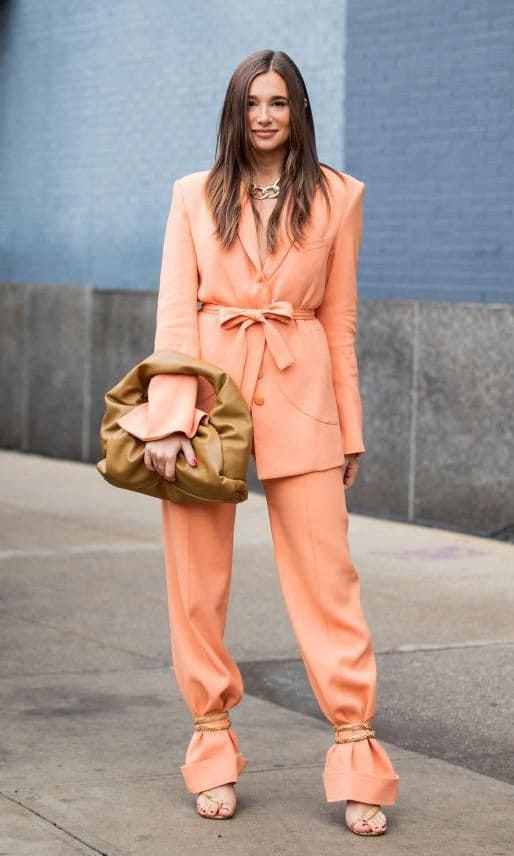 Danielle Bernstein in beige ankle strap sandals tied over the bottom of her orange pantsuit