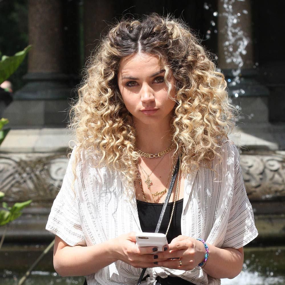 Ana de Armas poses with her phone in her hands rocking a curly blond look