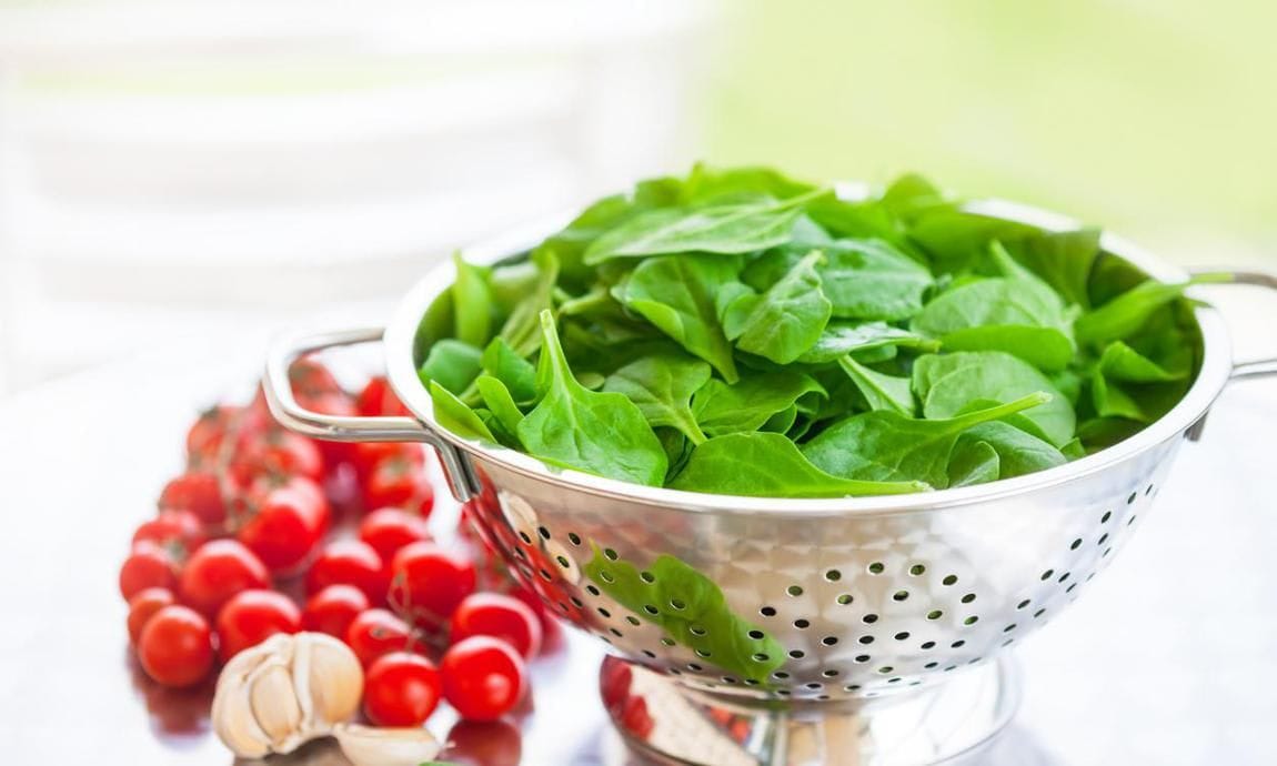 Garlic, cherry tomatoes, and colander with spinach leaves