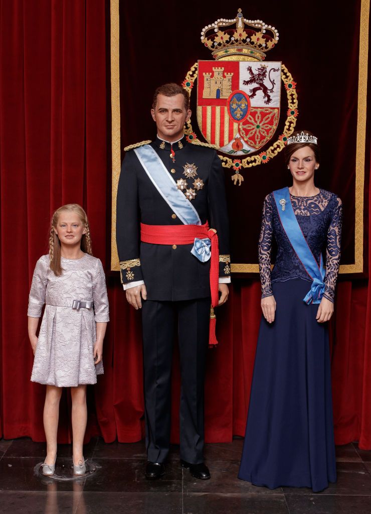 Wax figures of a young Princess Leonor, King Felipe VI in military attire, and Queen Letizia in a navy blue gown with a tiara, displayed at the Madrid Wax Museum.