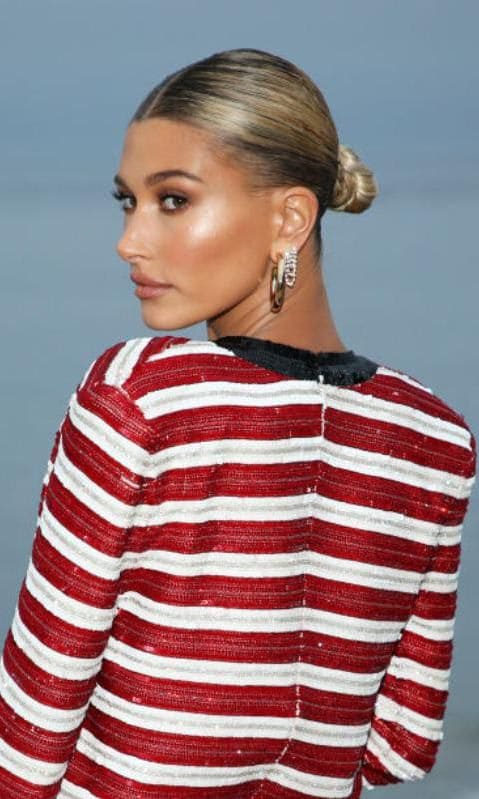 Hailey Baldwin con moño bajo, engominado y vestido de rayas