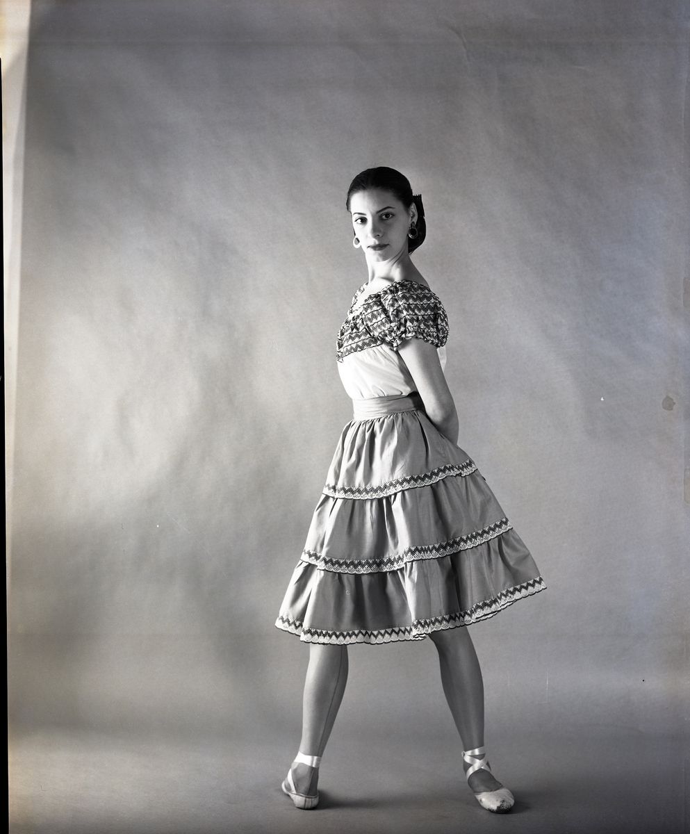 Portrait of ballet dancer Alicia Alonso wearing ruffled Mexican dress and pointe shoes, standing in ballet fourth position.