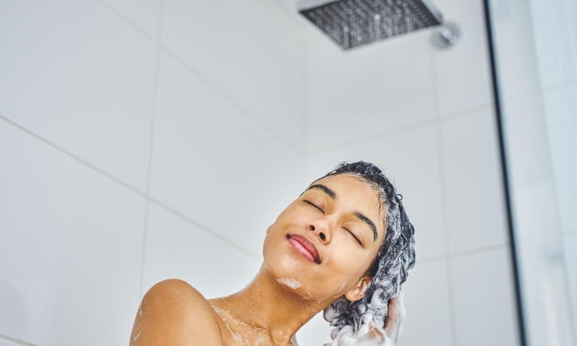 Shot of an attractive young woman washing her hair with shampoo in the shower at home