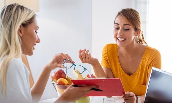 Young adult at a consultation with a nutrition professional, who is showing her a notepad, with food in the background