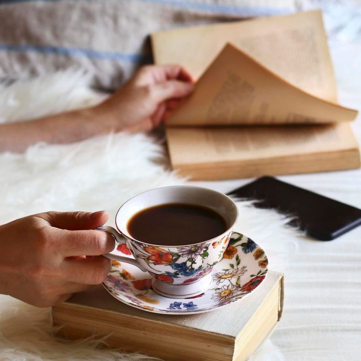 Female sitting on the bed, leafing through a book and drinking a cup of coffee