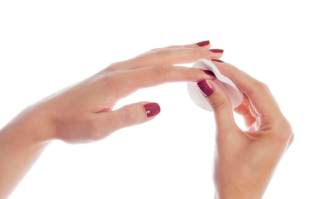 Woman removing lacquer from manicured nails with white cotton pad