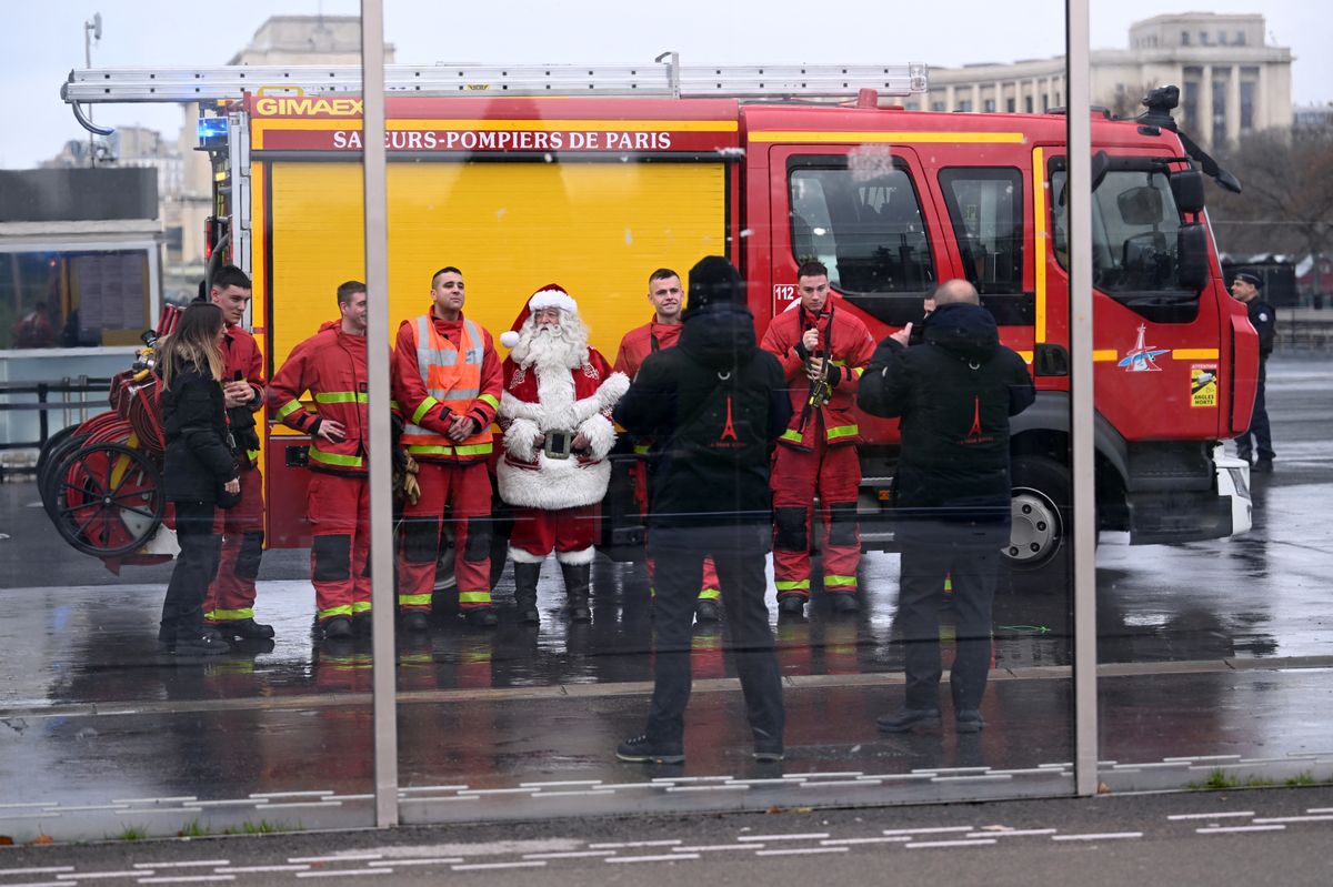 Firefighters pose for a picture with a Santa Claus near the Eiffel Tower as the site was closed and then reopened after a fire was reported in Paris, on December 24, 2024. (Photo by Anna KURTH / AFP) (Photo by ANNA KURTH/AFP via Getty Images)