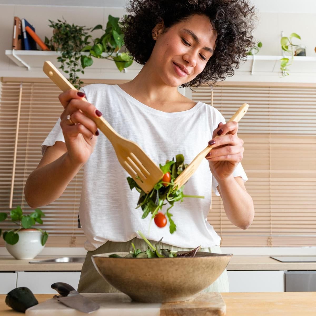 Happy young multiracial woman mixing bowl of fresh salad. Copy space.Healthy lifestyle concept.