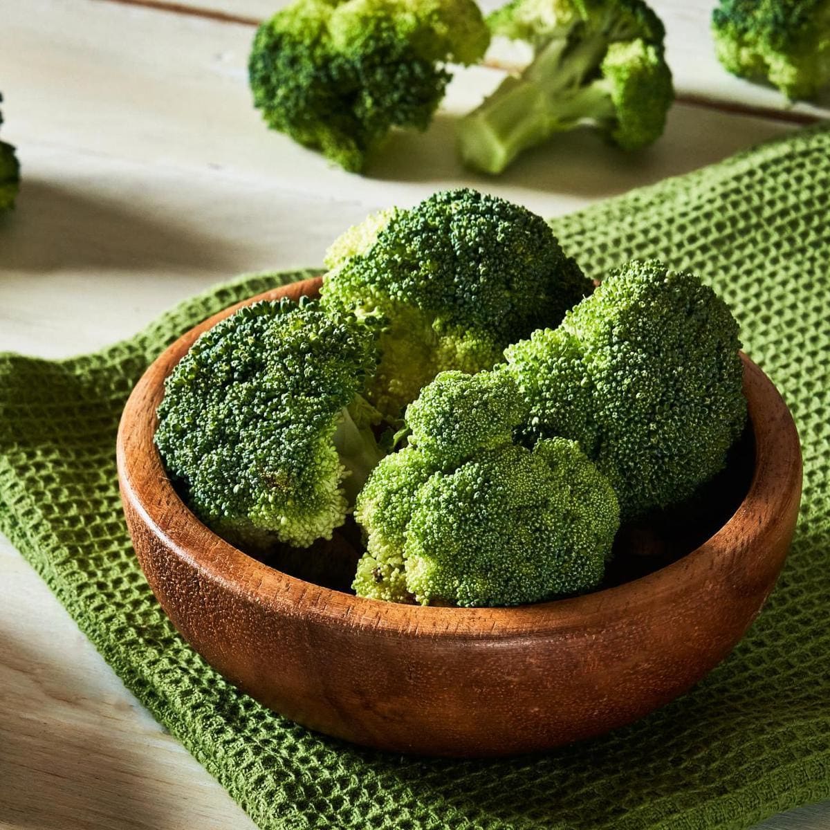 Fresh raw broccoli in bowl on rustic table.