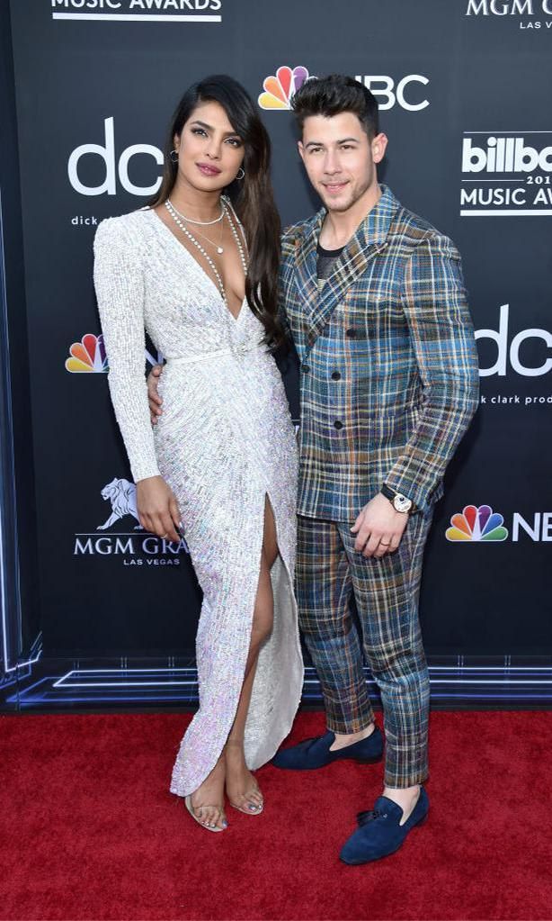 Proyanka Chopra in a sparkly white dress, low neck-line and split skirt and Nick Jonas in a tartan suit