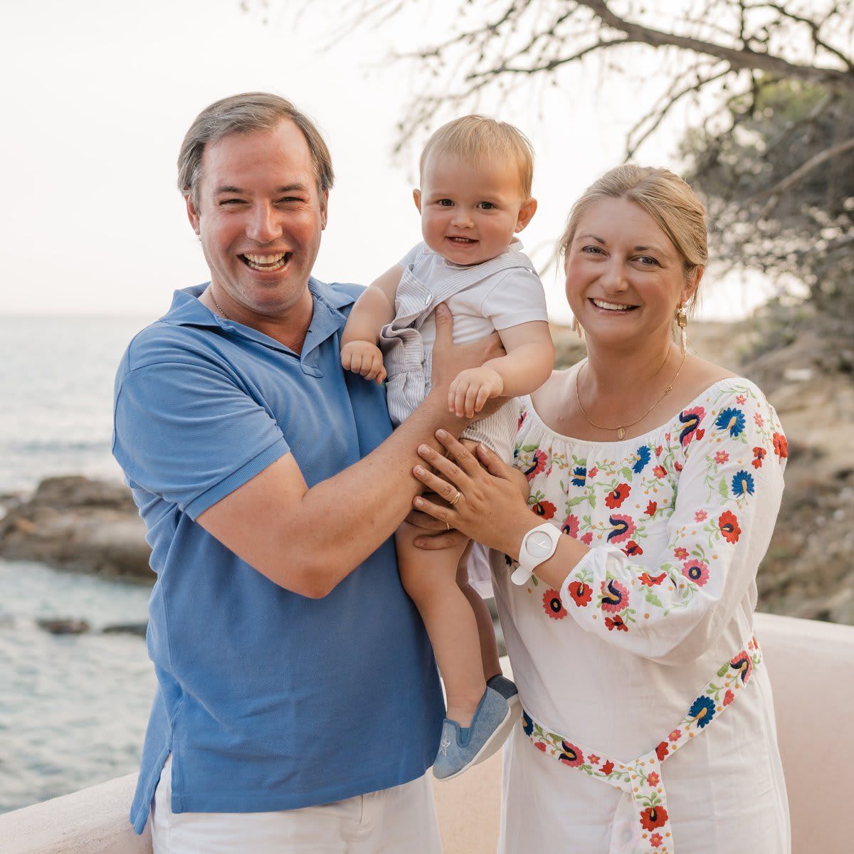 Hereditary Grand Duke Guillaume beamed holding his son alongside wife Hereditary Grand Duchess Stephanie, who looked summer-ready in a floral embroidered white dress.