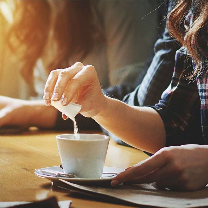 A woman sweetening a hot drink with artificial sweeteners