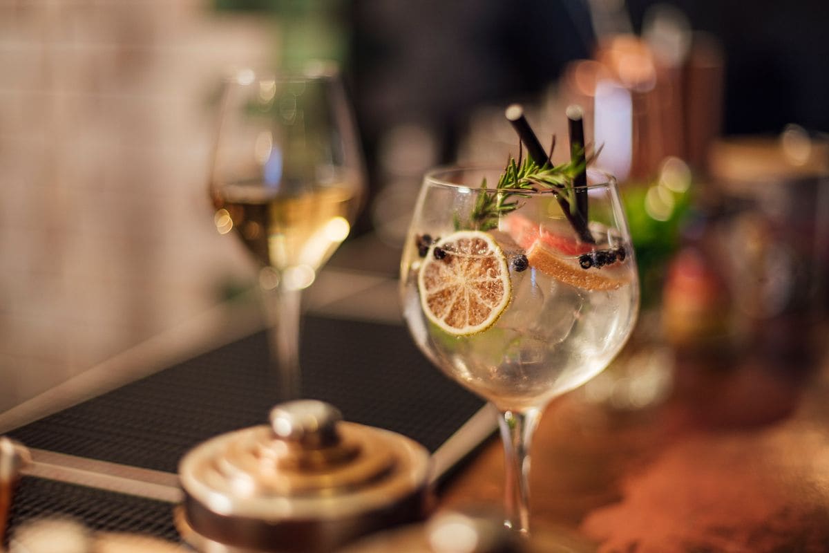 Close up shot of a freshly prepared gin and tonic served in a bowl glass standing on a bar counter. The drink is garnished with rosemary, grapefruit, and juniper berries.  The gastro pub is Located in Seahouses, Northumberland.