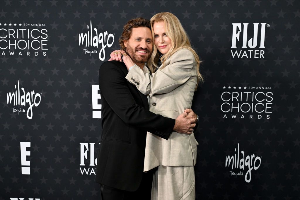 Nicole Kidman and Edgar Ramírez embrace on the red carpet at the 30th Critics Choice Awards, dressed in elegant tailored suits.