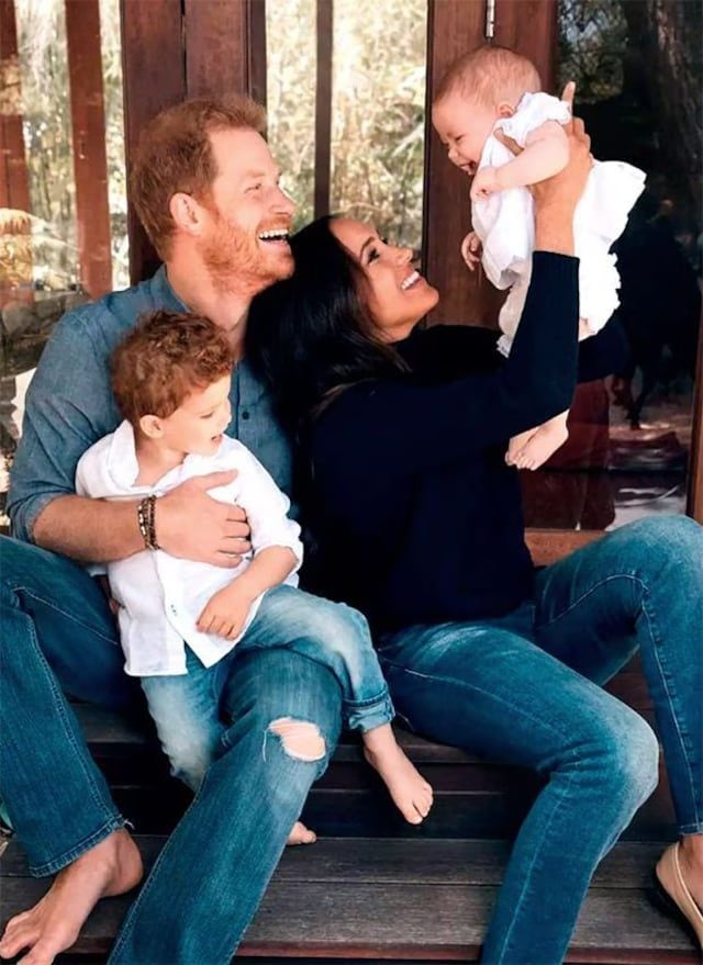 Prince Harry and Meghan Markle sit outdoors, laughing with their children, Archie and Lilibet. Harry holds Archie while Meghan lifts Lilibet in the air.