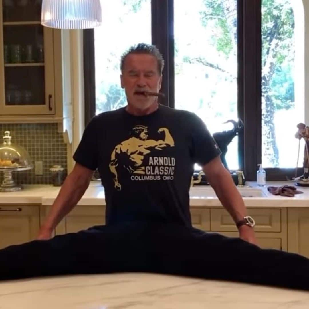 Arnold Schwarzenegger appears to do the splits on his kitchen counter while smoking a cigar